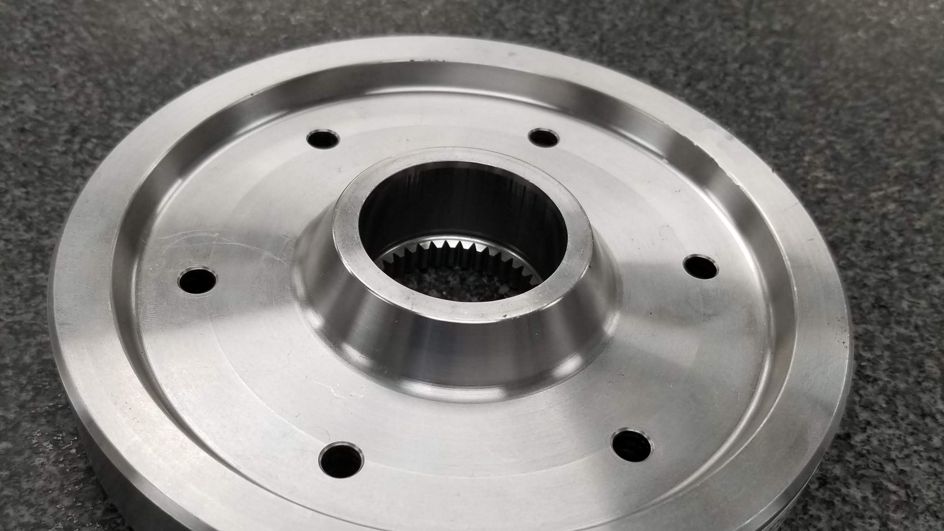 Close-up of a machined steel transmission driver flange with an internal spline and six drilled holes